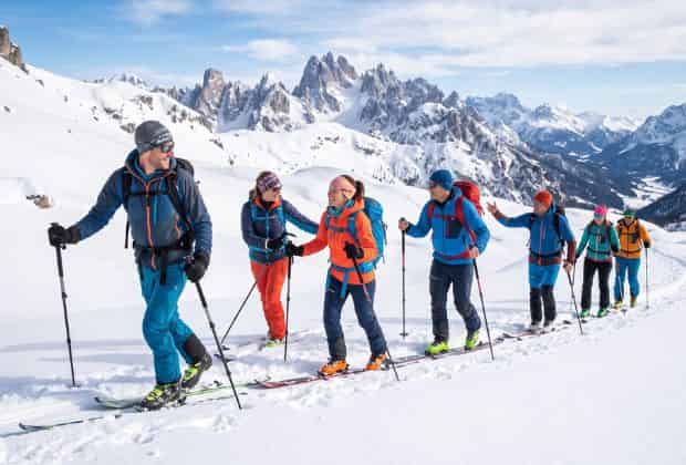 Un gruppo di colleghi che durante un team building scialpinisco salgono su una vetta innevata